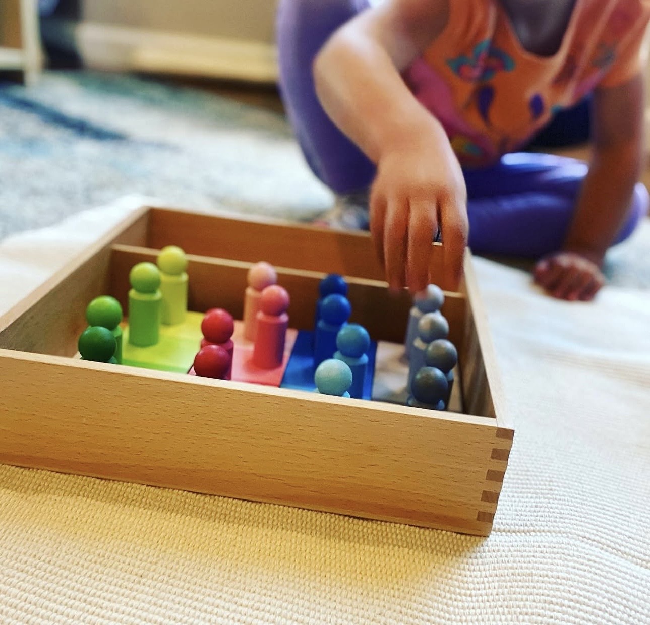 Child arranging colorful wooden Montessori peg dolls by hue